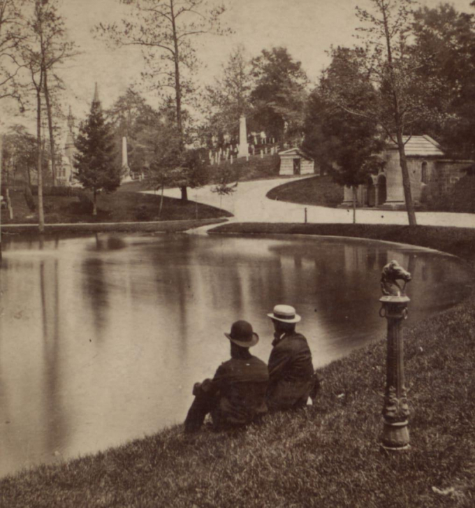 Two men seated by a serene pond in Green-Wood Cemetery