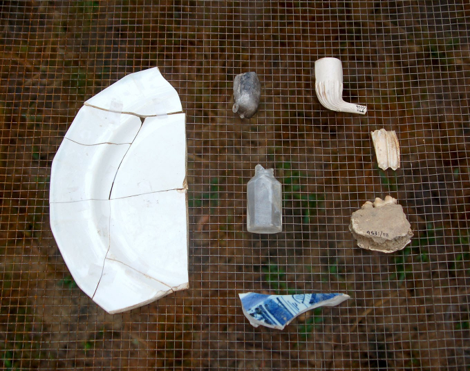 Excavated shards of kitchenware, a smoking pipe, and a bottle